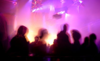 A Silhouette of people in a nightclub surrounded by pink and purple flashing lights